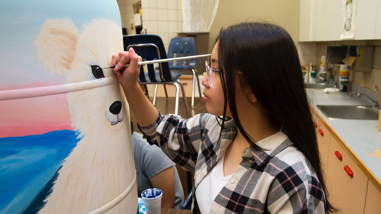Student puts finishing touches on one of several hand-painted barrels going up for auction in support of the Assiniboine Park Conservancy gardens.